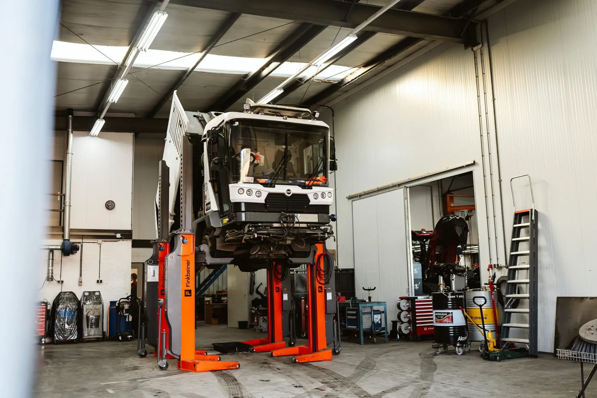 Witte veegmachine op mobiele hefkolommen in de werkplaats.