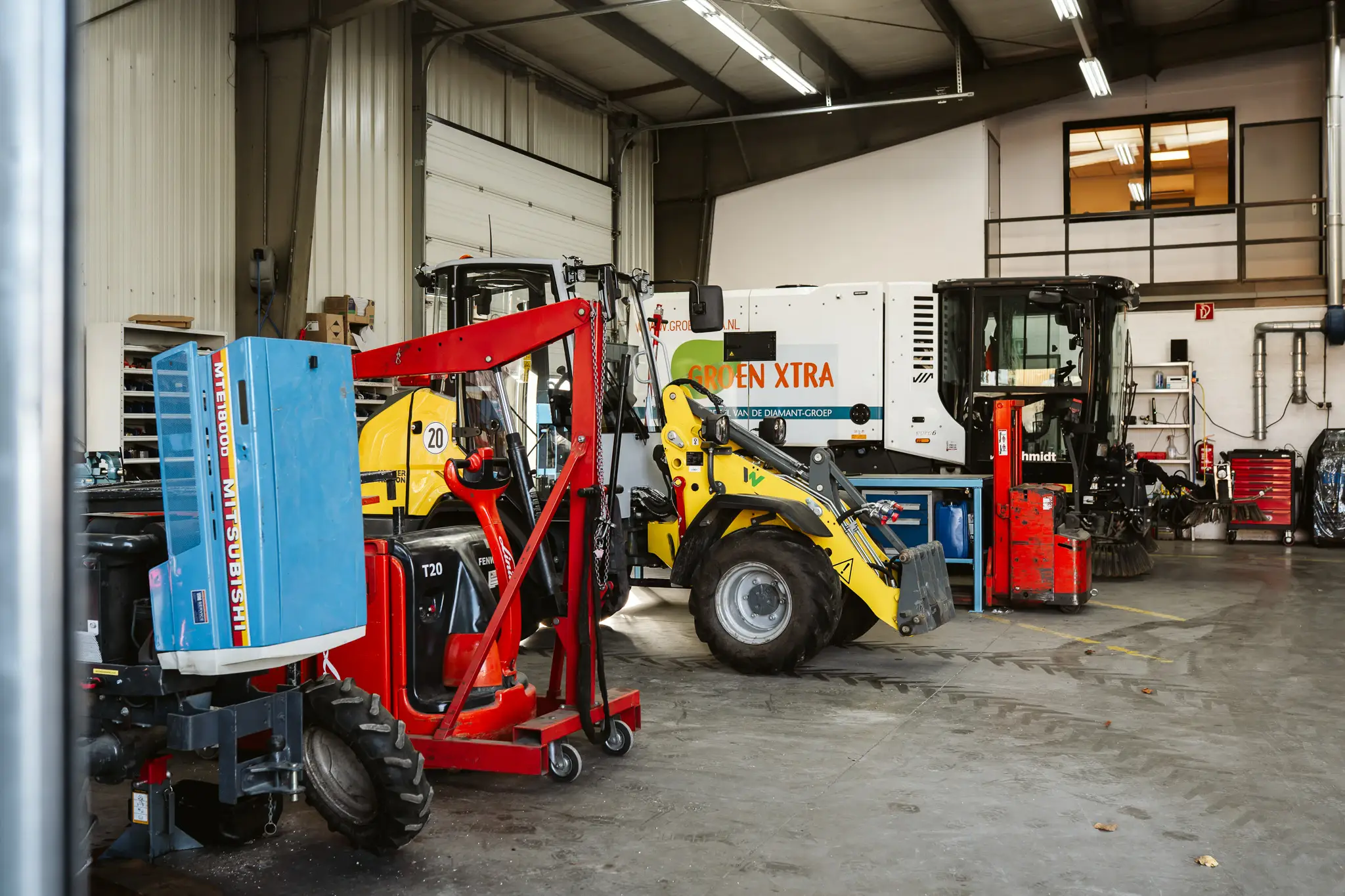 Heftruck, gele wiellader en veegmachine tussen het werkplaatsgereedschap.